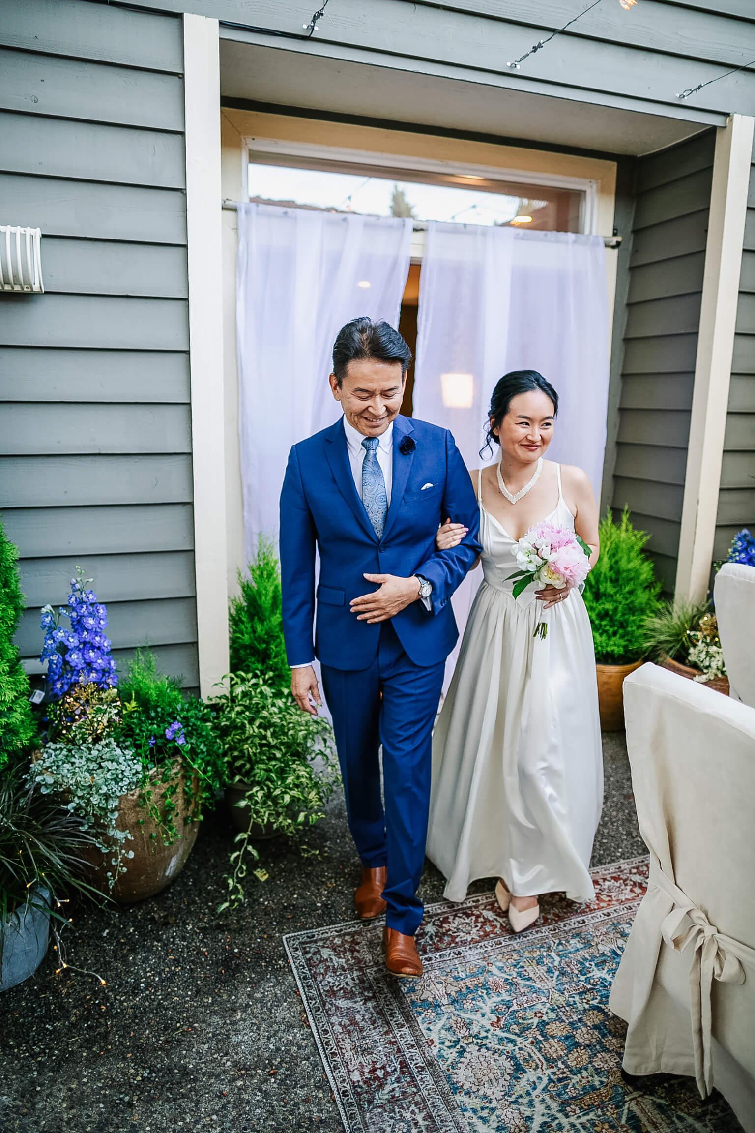 Rick dons a stunning blue suit and Lyanne wears a flowing white wedding dress. They link arms as they walk into the garden for Austin and Lyanne's wedding.
