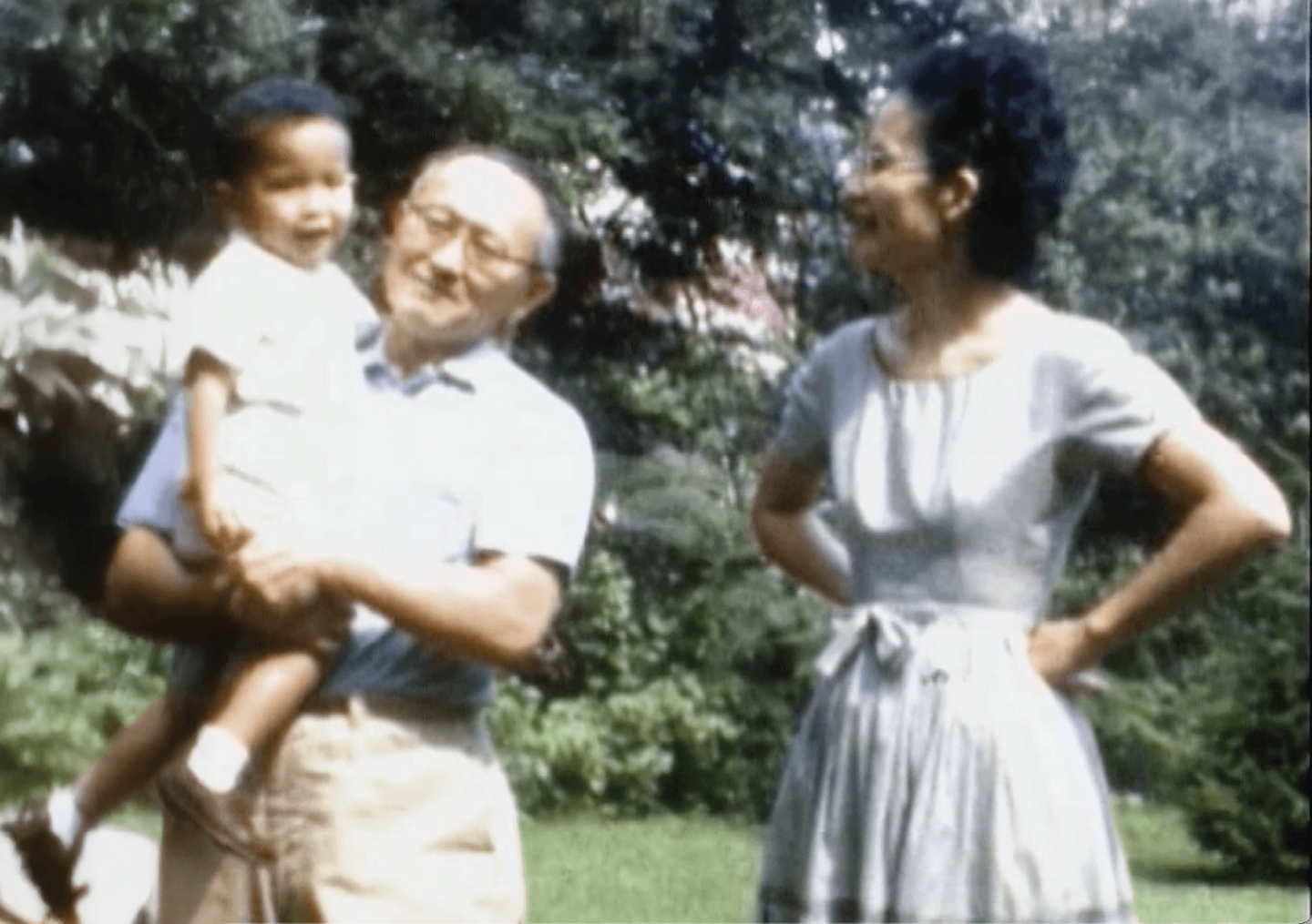 Dad holding Rick in his arms. Mom stands by their side, hands on hips, looking over at her family with a loving smile.