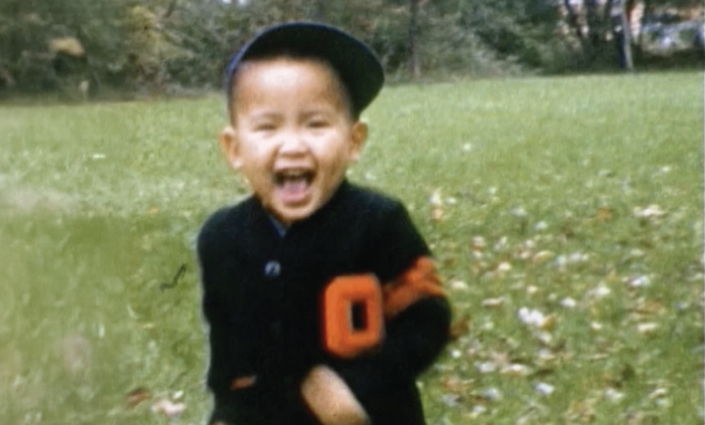 Rick as a happy little boy. He is outside, running around in a field of grass. His giant open smile beams with joy.